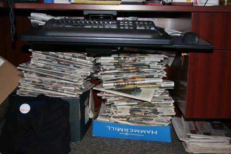 Keyboard supported by stacks of newspapers under desk.